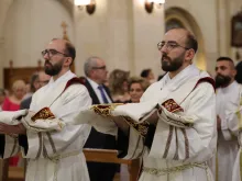 The entrance into the Franciscan church in Aleppo, Syria, of the twins George and Johnny Jallouf, friars of the Custody of the Holy Land, who were ordained priests on July 6, 2024. The two ordinands are wearing the priestly vestments with which they were clothed during the ordination rite. They were 15 when the war in Syria broke out. Their vocation was born and grew amid the Battle of Aleppo. “I tried to attend Mass every day,” George recounted. “I was afraid, but I kept repeating to myself ‘I fear nothing because you are with me.’ This phrase guided me, reassured me, gave me peace.”