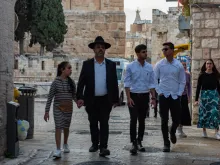 A family of religious Jews walks at the beginning of Armenian Quarter Street, the entry point to the Armenian Quarter of Jerusalem in April 2024. Behind them stands the complex of the Tower of David Museum.