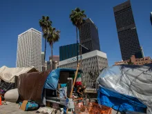 A homeless man fixes his bike outside his tent next to the 110 Freeway in Los Angeles California on May 25, 2020.